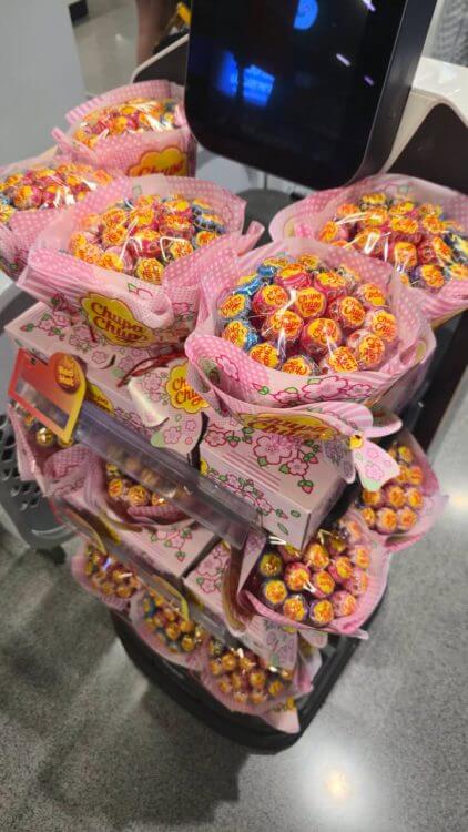 ช่อดอกไม้ลูกอม Chupa Chups หลายช่อเรียงอยู่ในรถเข็นจำหน่ายในซูเปอร์มาร์เก็ต