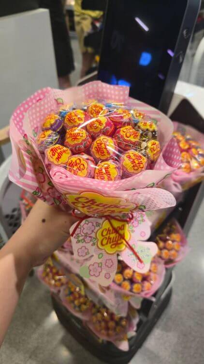 มือถือ Chupa Chups Bouquet ช่อดอกไม้ลูกอมห่อกระดาษชมพูลายดอกไม้ใกล้ๆ