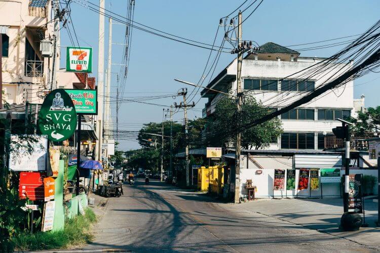 A bustling urban street in Chiang Mai, Thailand showcasing shops, power lines, and signages.
