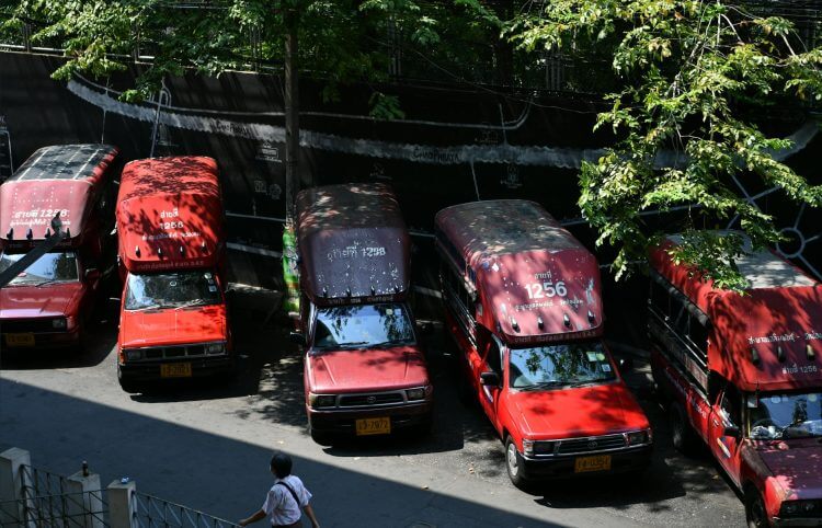 Aerial view of red songthaews parked in a shaded urban area with a pedestrian passing by.