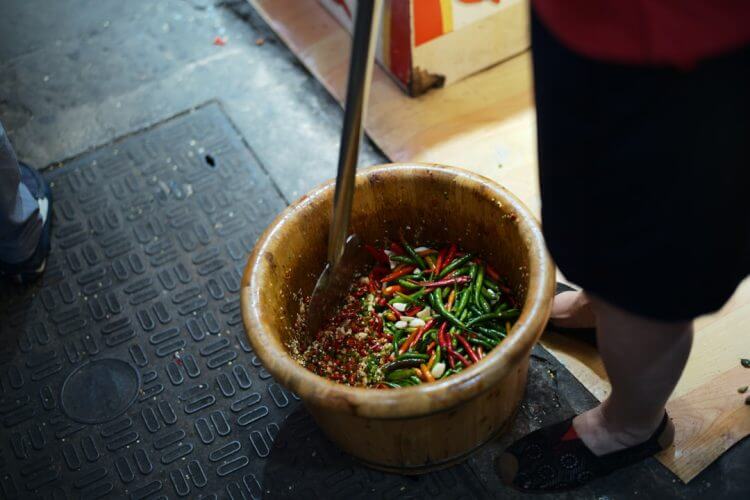 Person preparing food in a large mortar and pestle.