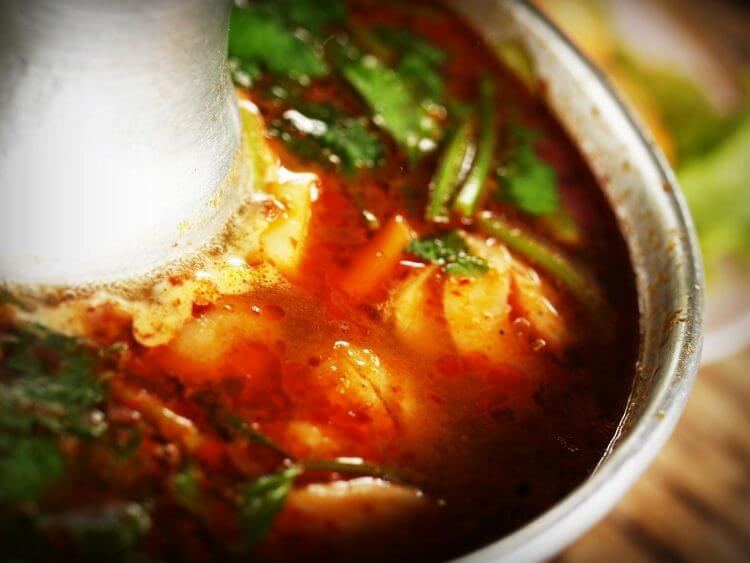 Close-up of flavorful Thai Tom Yum soup with aromatic herbs in a metal bowl.