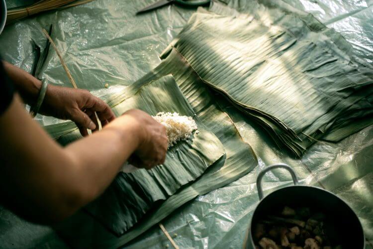 Close-up of hands preparing Banh Tet with rice and banana leaves.