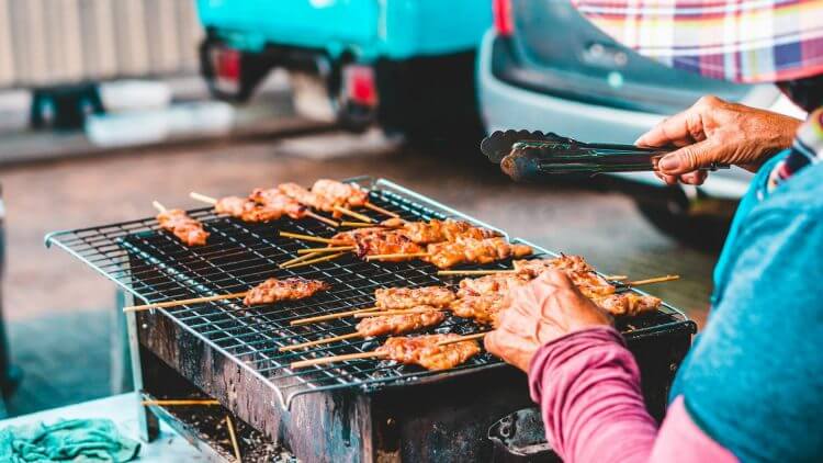 Delicious skewered meat grilling at a street food stall in Bangkok, Thailand.