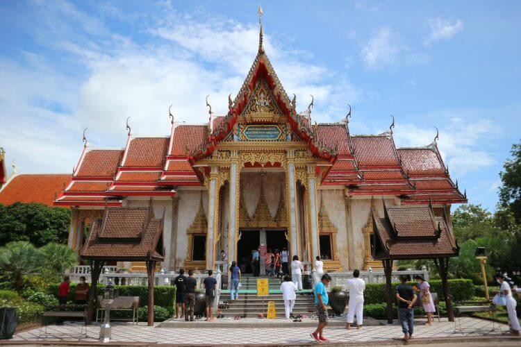 Visitors exploring the stunning Wat Chalong Temple in Phuket, Thailand, on a sunny day.