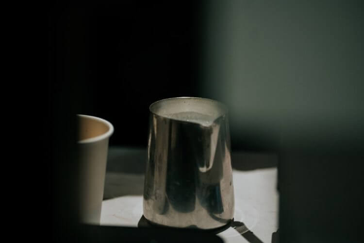 Metal pitcher and paper cup on tray.