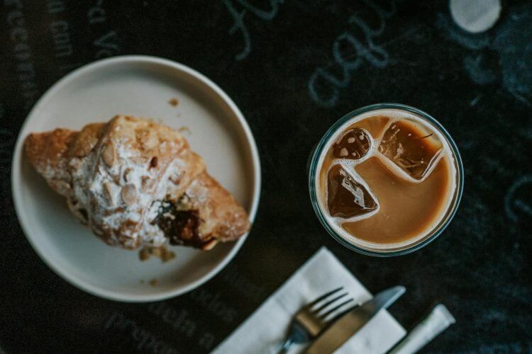Flat lay of a croissant and iced coffee on a dark table, creating a cozy café vibe.