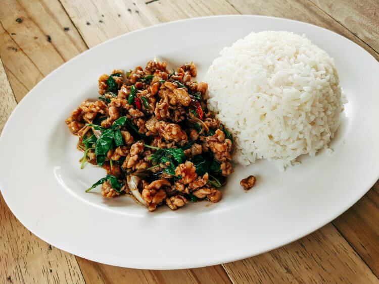Authentic Thai stir fry with pork, basil, and rice, served on a rustic wooden table.