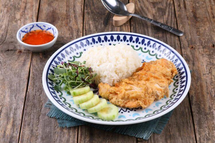 Thai-style fried chicken with rice and salad on a decorative plate.