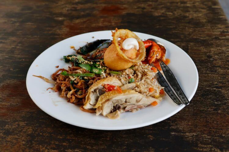 A plate of diverse food with chicken and fried onions.