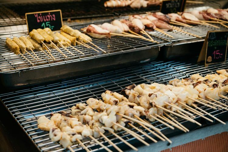 Close-up of skewered street food items in a Bangkok market stall.