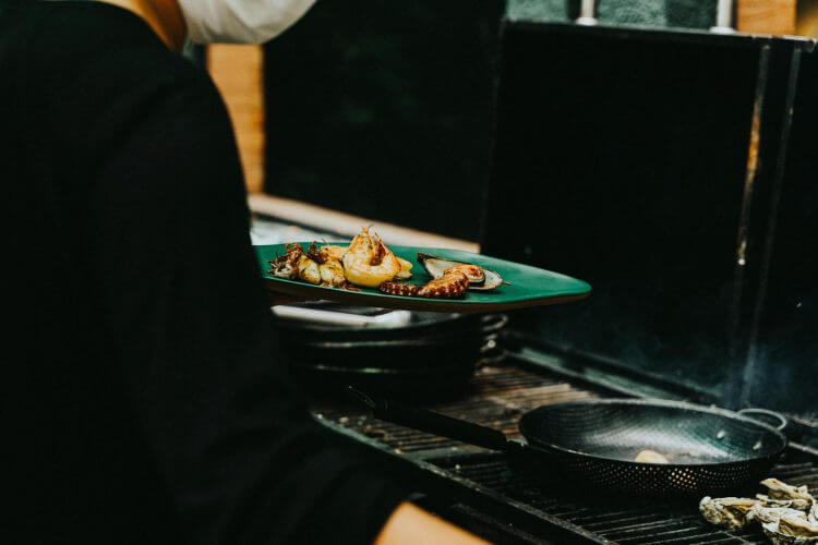 Chef preparing grilled seafood on a stove, featuring octopus and mussels. Indoor culinary scene.