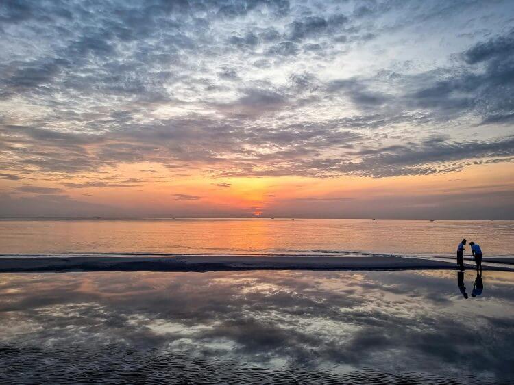 Peaceful sunrise over Hua Hin Beach with reflections in the calm water, capturing serene beauty.