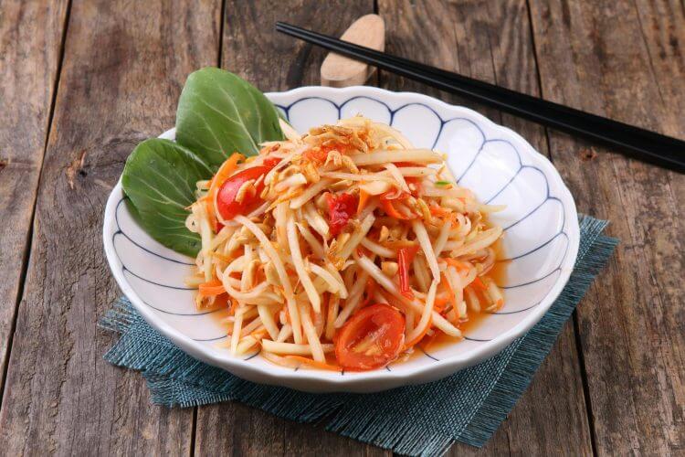 Delicious Thai papaya salad with fresh ingredients served on a wooden table.