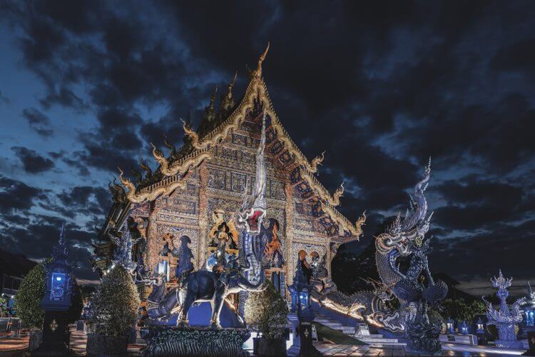 Ornate temple illuminated at night under cloudy sky