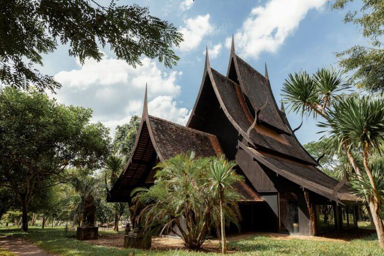 Traditional dark wooden house surrounded by lush green trees.