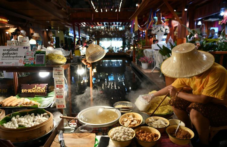 Thai street vendor preparing noodles at a vibrant indoor market stall.