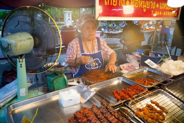 Elderly woman prepares food at a street stall.