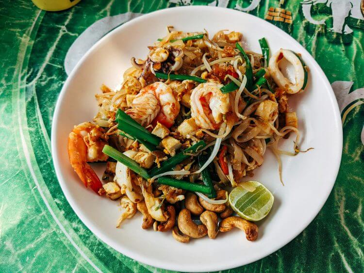 Close-up of Pad Thai with shrimp, vegetables, and lime served on a ceramic plate in Bangkok.