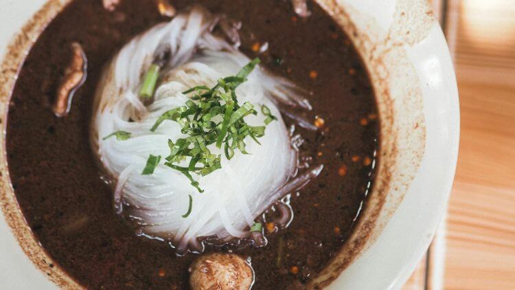 Close-up of a traditional Thai noodle dish with fresh herbs in a rich, dark broth.