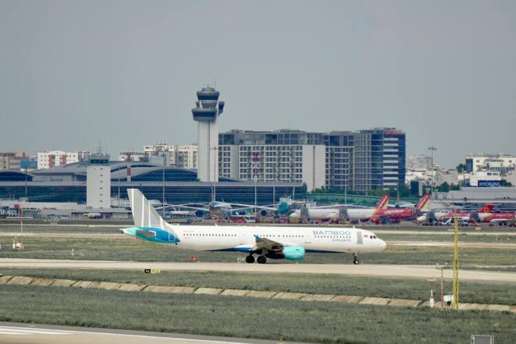 A Bamboo Airways plane on the runway at a busy airport with control tower.