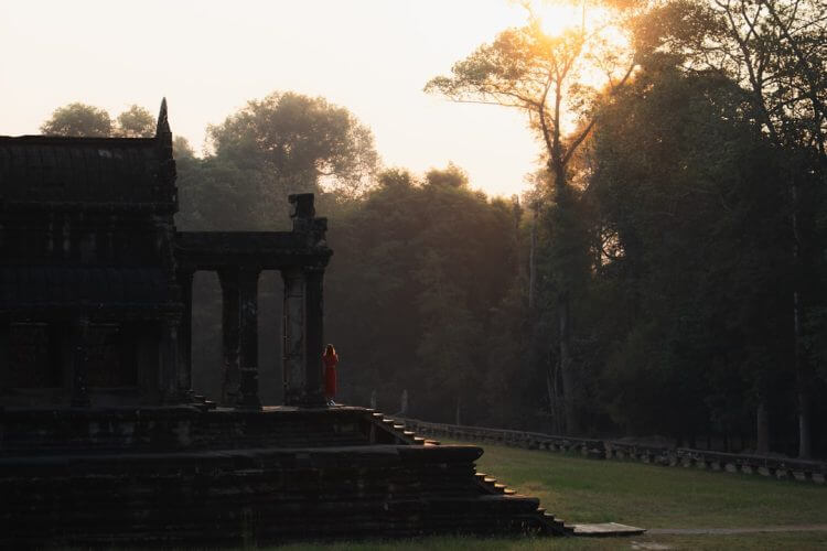 Monk walks up steps of ancient temple at sunrise.