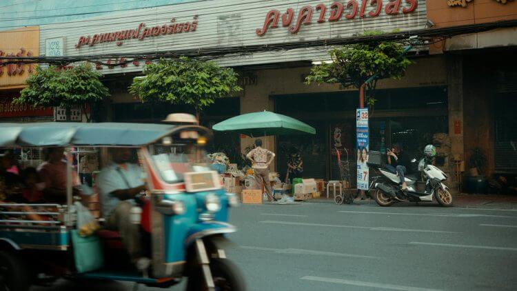 A lively urban scene with a tuk-tuk passing by a traditional storefront, capturing city life.