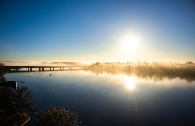 the sun is setting over a lake with a bridge in the background