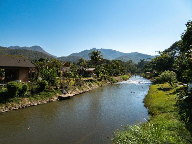 Tranquil riverside village nestled in lush mountains under a clear blue sky.