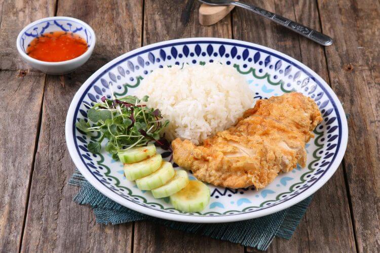 Plate of fried chicken, rice, and vegetables with sauce on a rustic table.