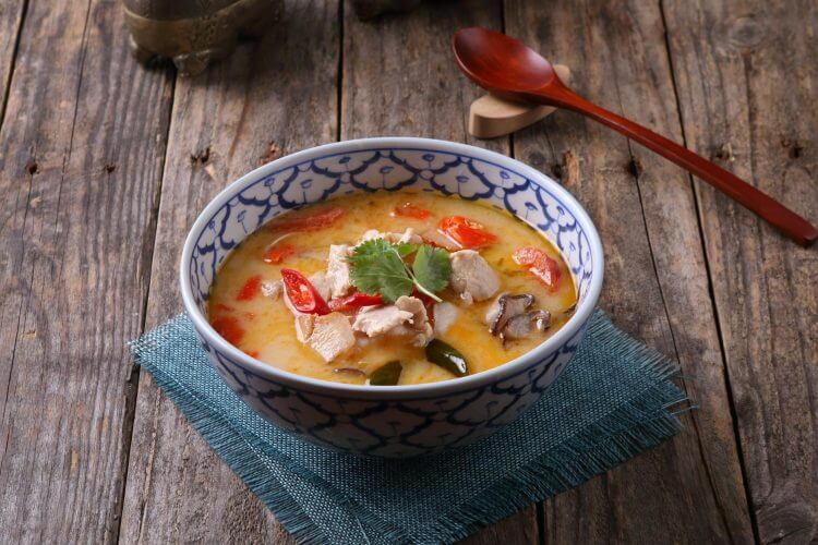 Tom Kha Gai soup with chicken and vegetables, served in a traditional Thai bowl on rustic wooden table.