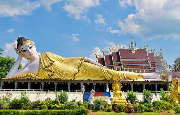 Stunning view of a golden Reclining Buddha statue against a vivid blue sky in Thailand's beautiful temple grounds.