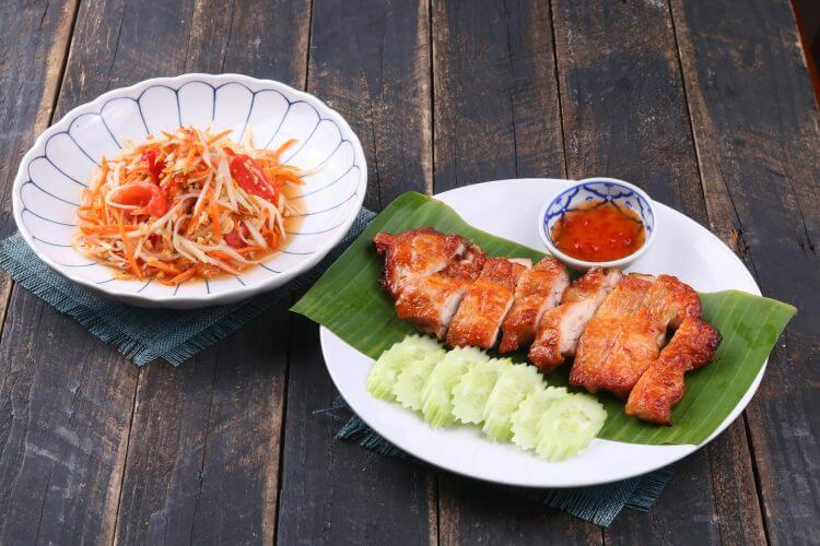 Authentic Thai grilled chicken with spicy papaya salad on a rustic wooden table.
