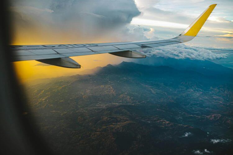 Airplane wing over scenic landscape with dramatic clouds at sunset, showcasing aerial travel view.