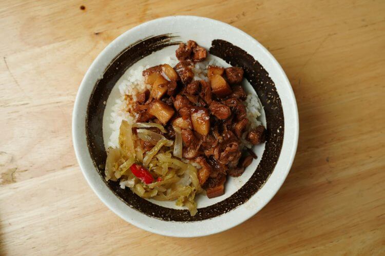 A savory bowl of braised pork with rice and vegetables on a wooden table.