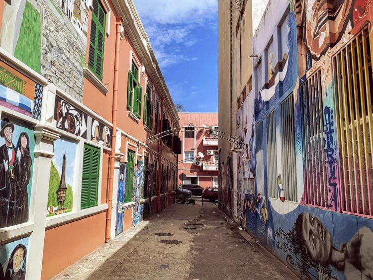 Explore a narrow alley adorned with colorful murals in a vibrant urban setting, inviting artistic exploration.