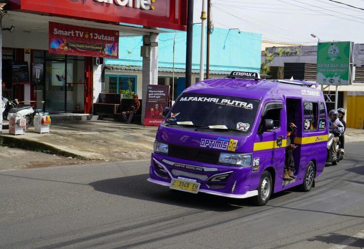 Vibrant purple public minibus drives on a busy street in West Java, Indonesia, showcasing local urban life.