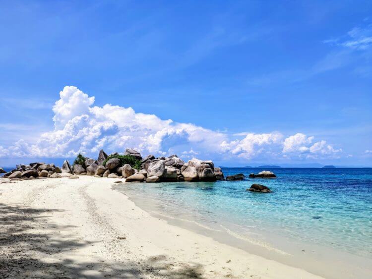 a beach with rocks and clear water under a blue sky