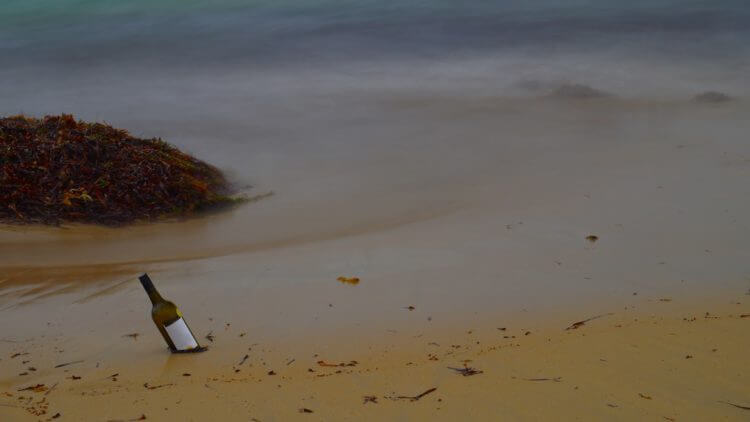 A bottle on a sandy beach with gentle waves.
