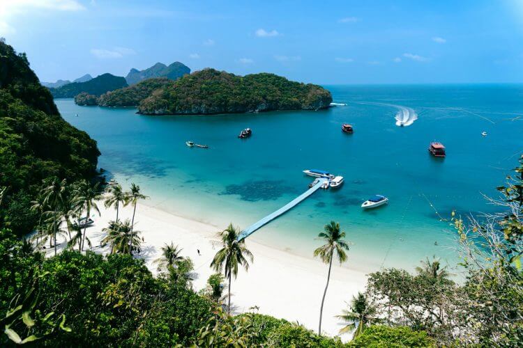 Stunning aerial view of a tropical beach with boats and lush islands under a clear sky.