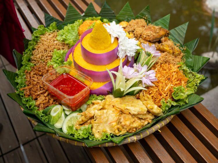 A vibrant display of Indonesian Tumpeng rice surrounded by various traditional side dishes and garnishes.