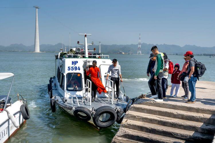 A group of tourists boards a motorboat at a picturesque harbor with cable towers in the background.