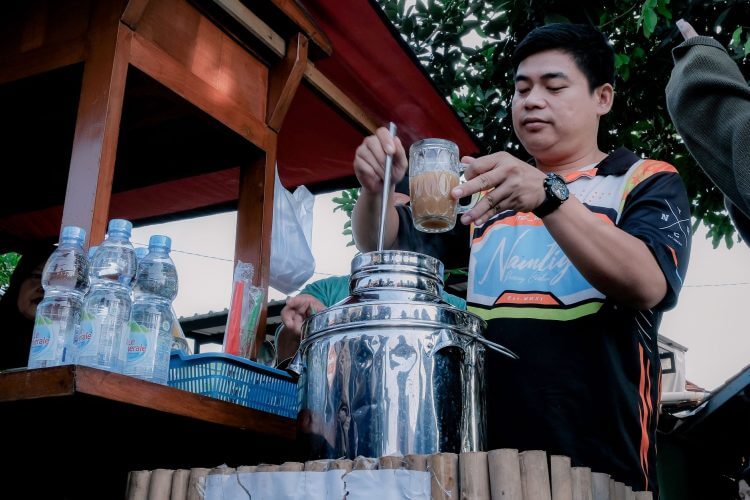 Man at West Java street stall making a traditional Indonesian beverage outdoors.