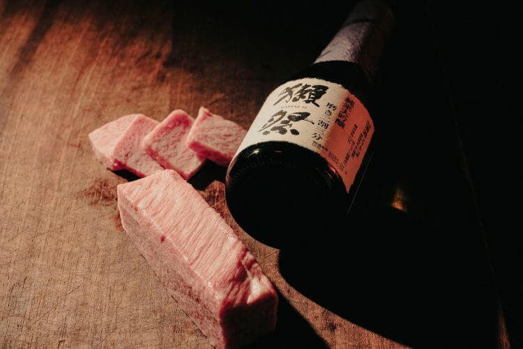 Sliced Wagyu beef paired with a bottle of premium Japanese sake, artistically presented on a wooden surface.