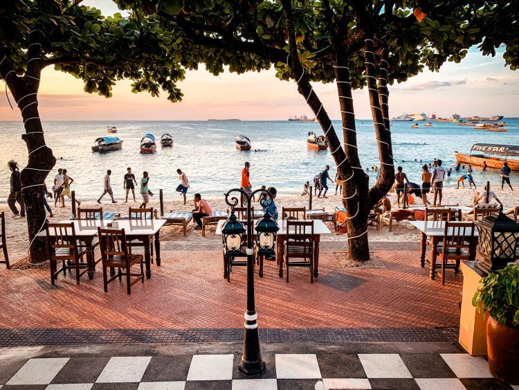 Charming beachside dining setup at sunset with people enjoying the ocean view.