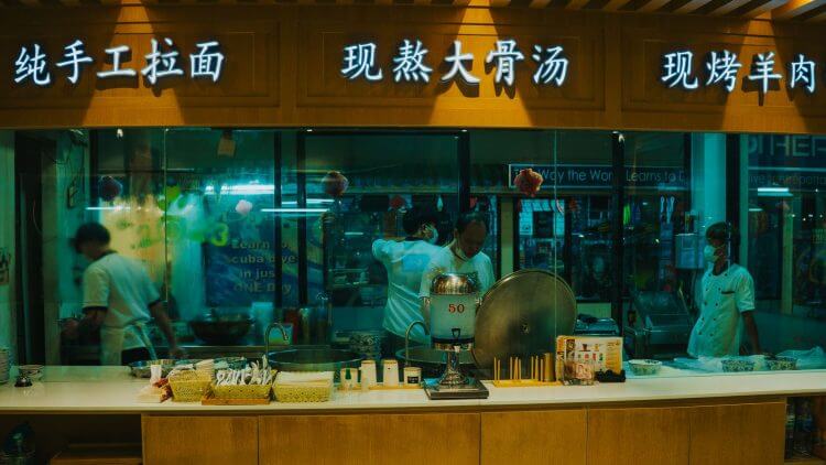 Chefs prepare traditional dishes at a bustling Bangkok noodle shop, showcasing authentic cuisine.