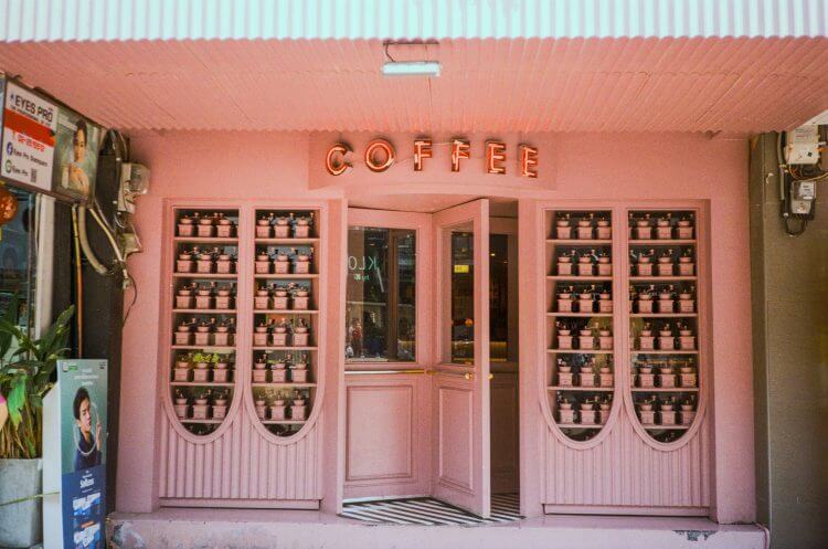 Pink exterior of a trendy coffee shop in Bangkok with neon signage.