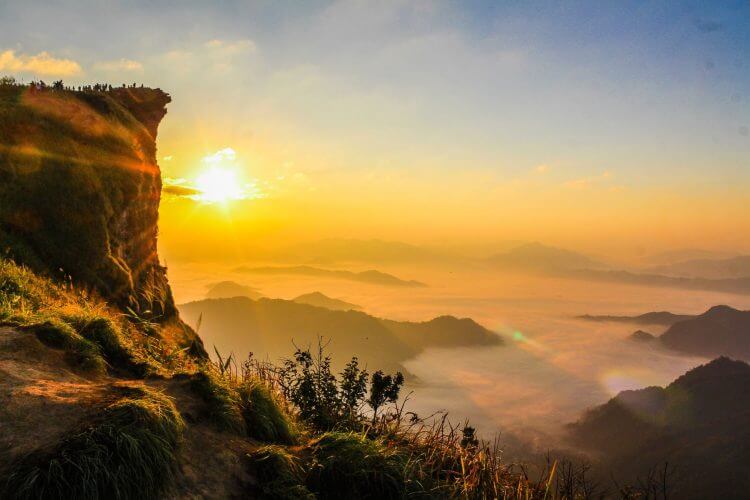 Breathtaking view of sunrise with mist and green cliffs, capturing nature's beauty.