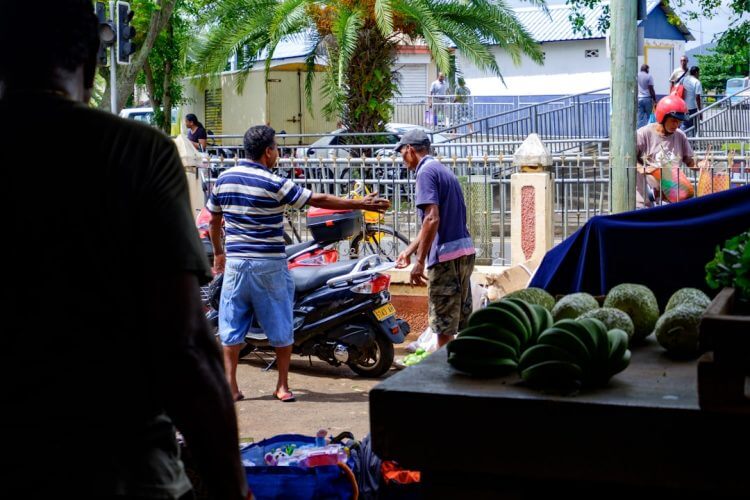 Men interacting at an outdoor market stall with produce.