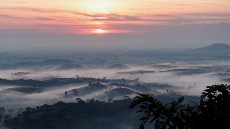Serene sunrise over misty hills in Chiang Rai, Thailand, creating a tranquil landscape.